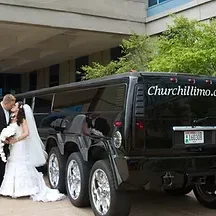 Wedding couple posing beside a black multi‑axle stretch limousine used for wedding transportation.
