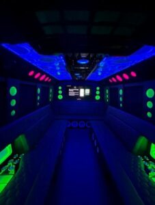 Interior of a party bus with neon LED lighting and lounge seating.